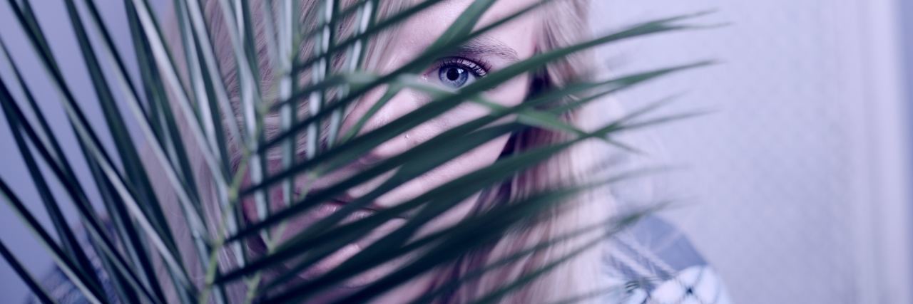 photo of young woman looking out from behind palm leaf