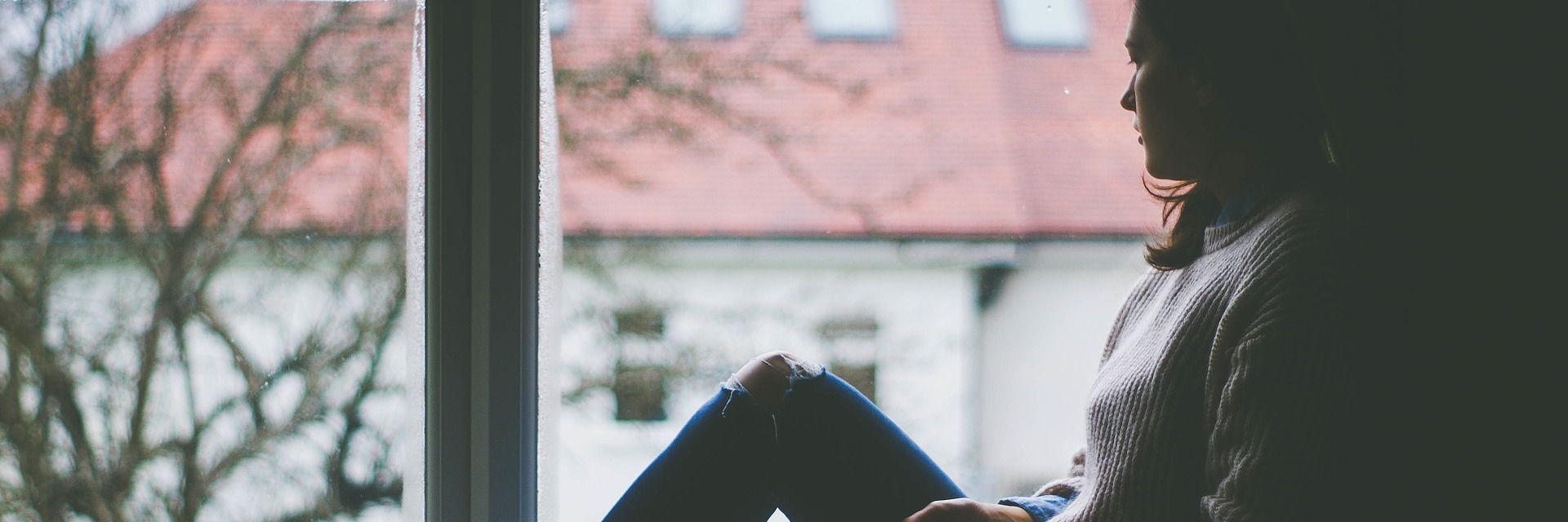 Surprising Lessons I Learned From the Mental Hospital young woman looking out of window with building and tree outside