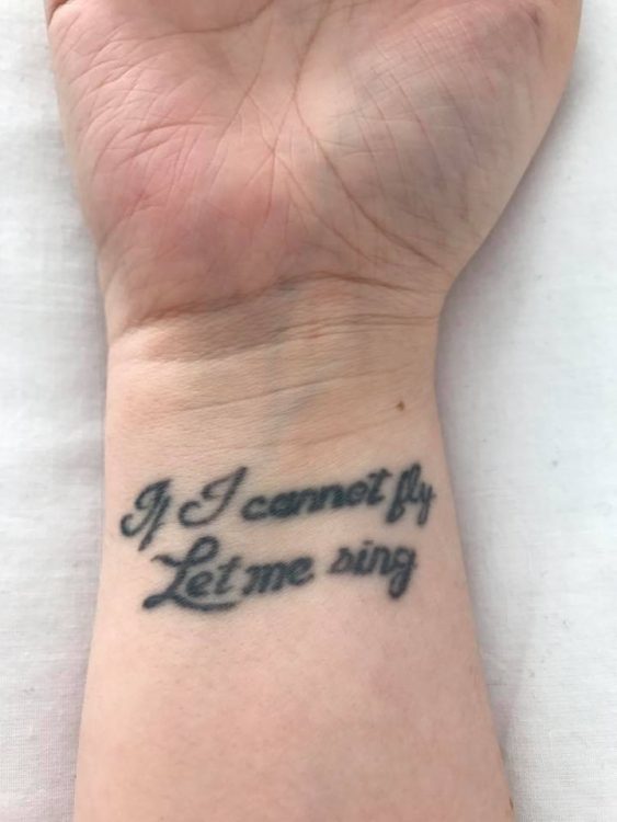woman with tattoo on her wrist that says 'if I cannot fly, let me sing'
