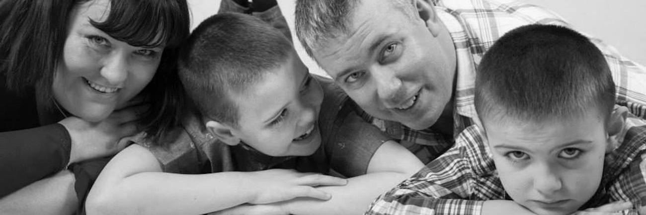 A Letter to Myself Regarding My Sons' Autism Diagnoses Black and white family portrait, mom, son, dad, son, laying on their stomachs, closeup of their faces