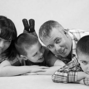 Black and white family portrait, mom, son, dad, son, laying on their stomachs, closeup of their faces