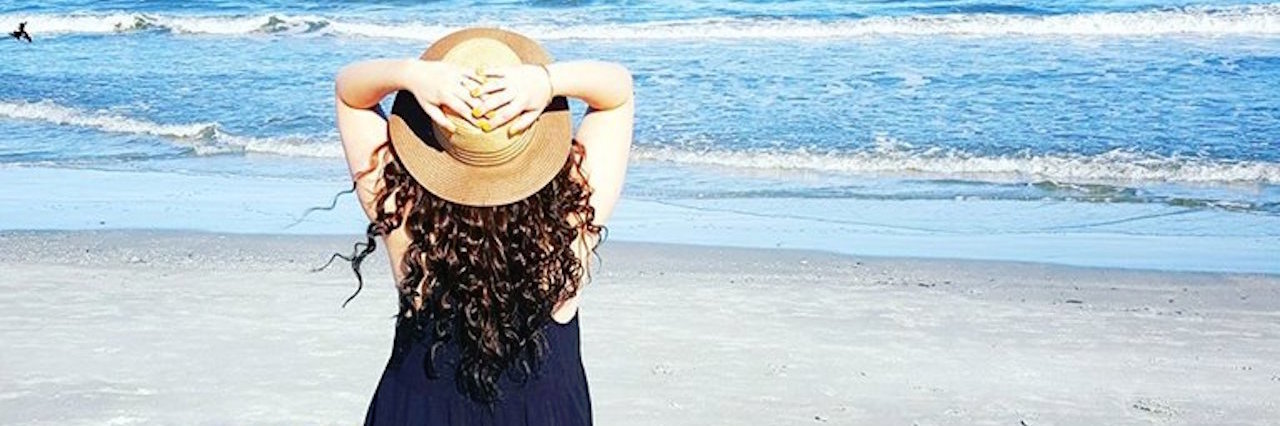 Tips for Traveling, Going on Vacation With Endometriosis woman standing on the beach in a black sundress and hat
