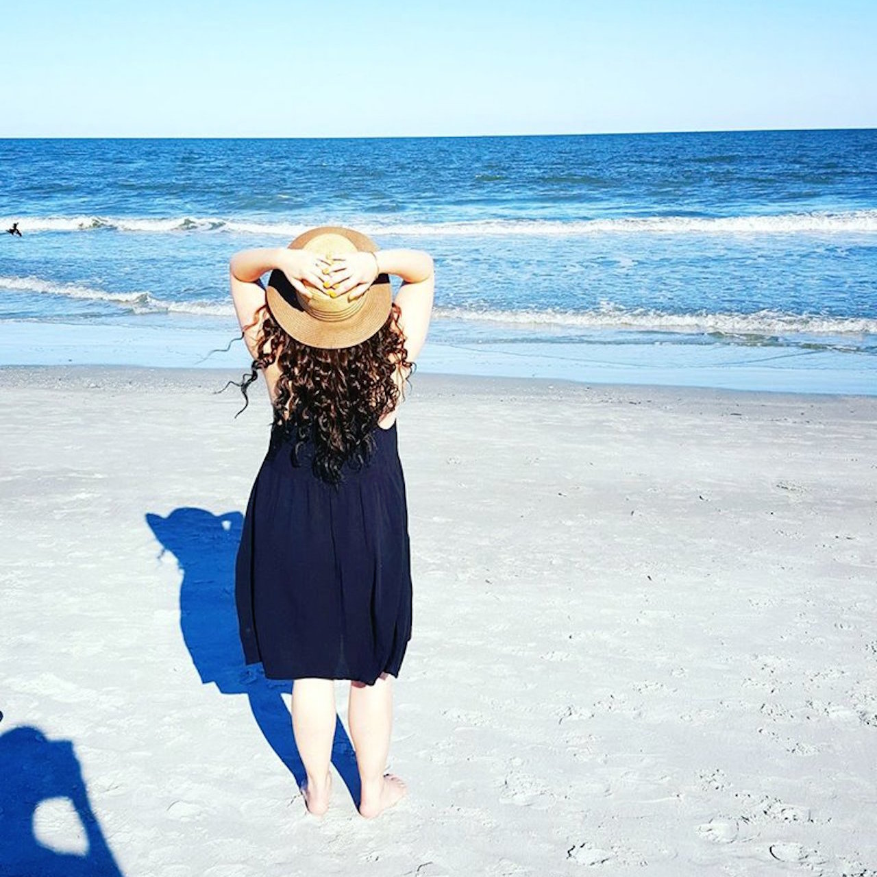 woman standing on the beach in a black sundress and hat