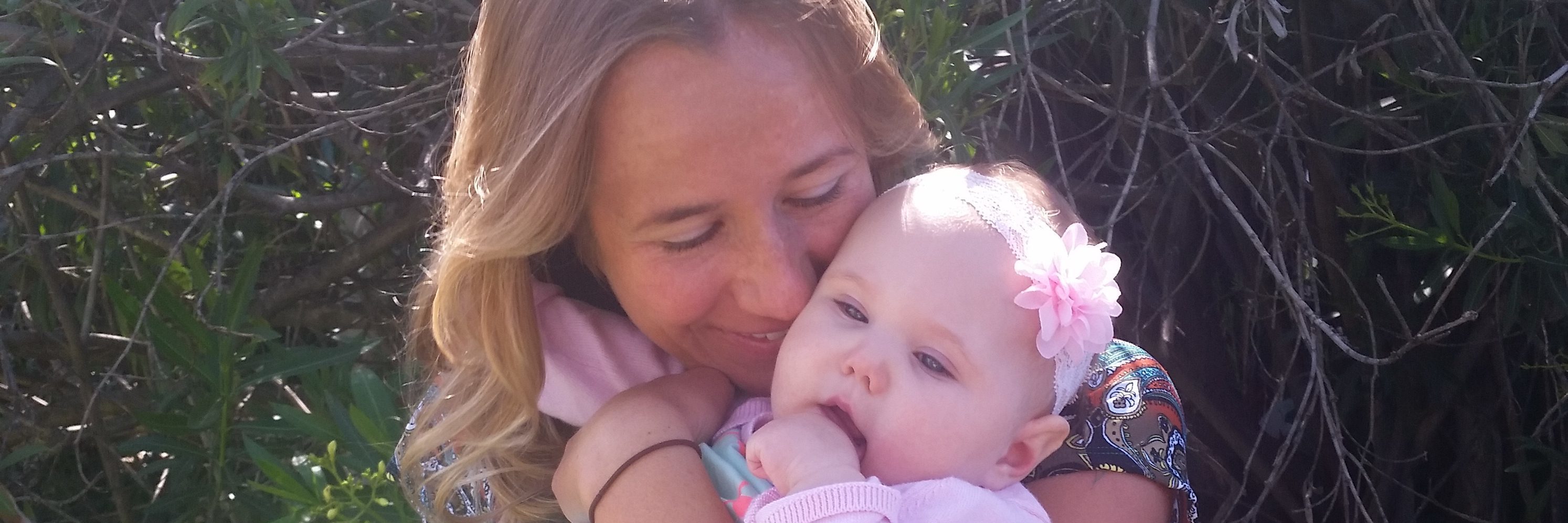 To the Mom With a Child Who Uses a Wheelchair, I Apologize A mother wearing a blue dress holding her baby daughter who wears a pink sweater and teal dress.