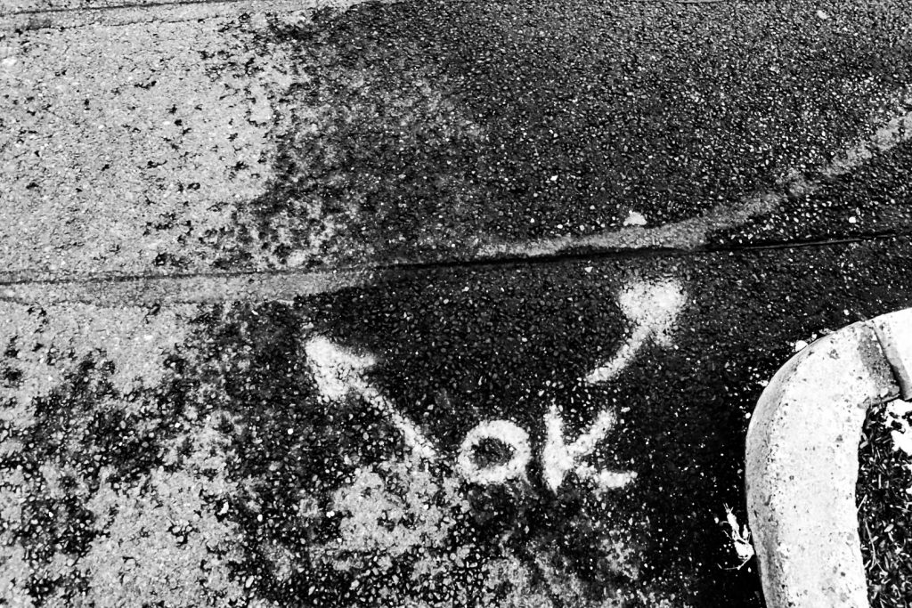 black and white photo of crack on ground with OK written on ground and two arrows pointing at crack