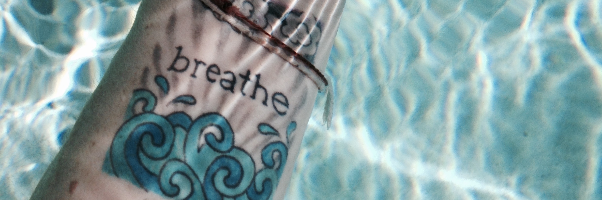 woman's hand under water with a tattoo on her wrist that says 'breathe'