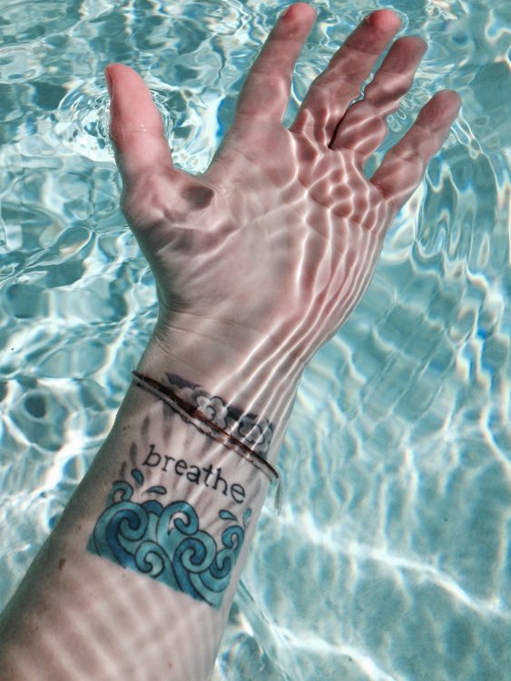 woman's hand under water with a tattoo on her wrist that says 'breathe'