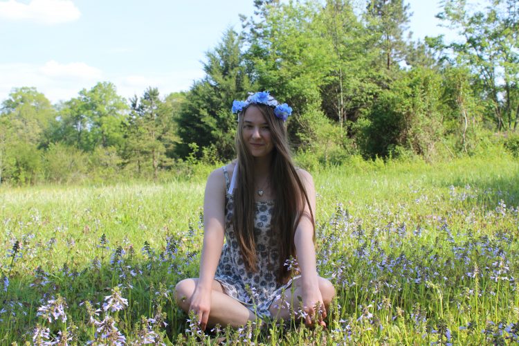 woman wearing flower crown and sitting cross-legged in a field