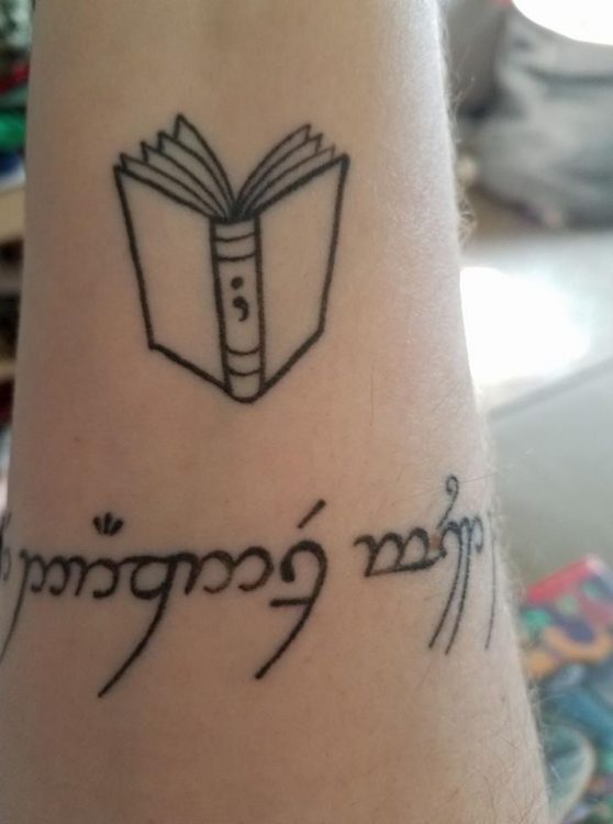book with semicolon and elvish script tattoo on arm