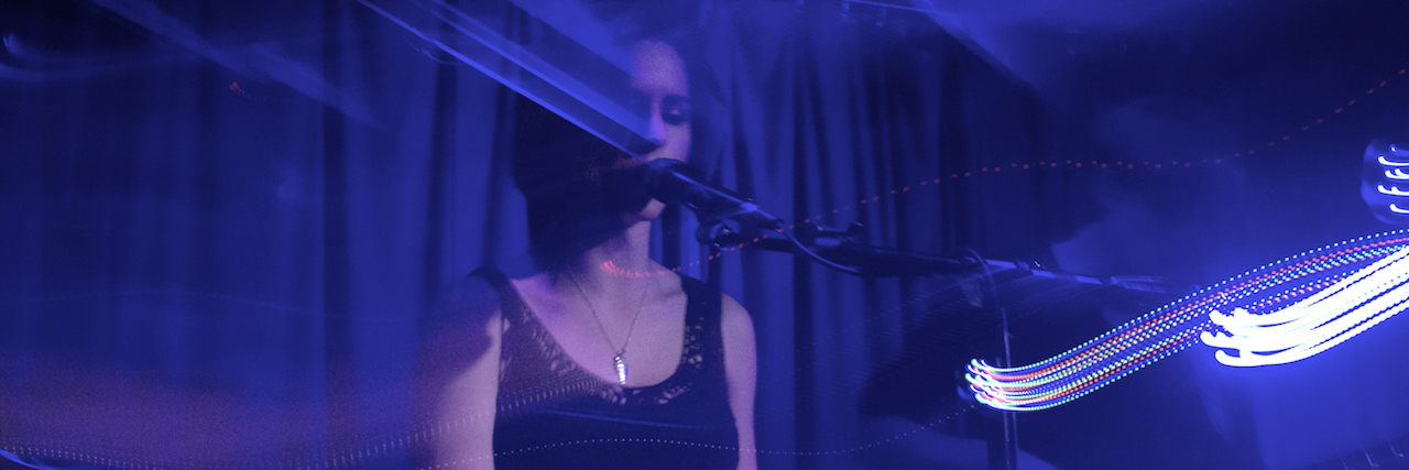 How Bipolar Disorder Helps Me Write Music a woman playing piano and singing on a dark stage