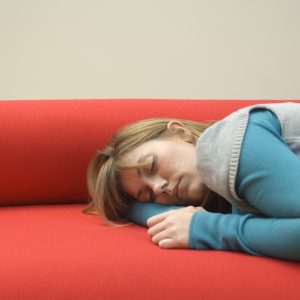 A woman sleeps on a red sofa.