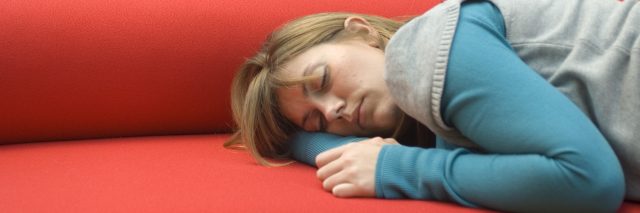 A woman sleeps on a red sofa.