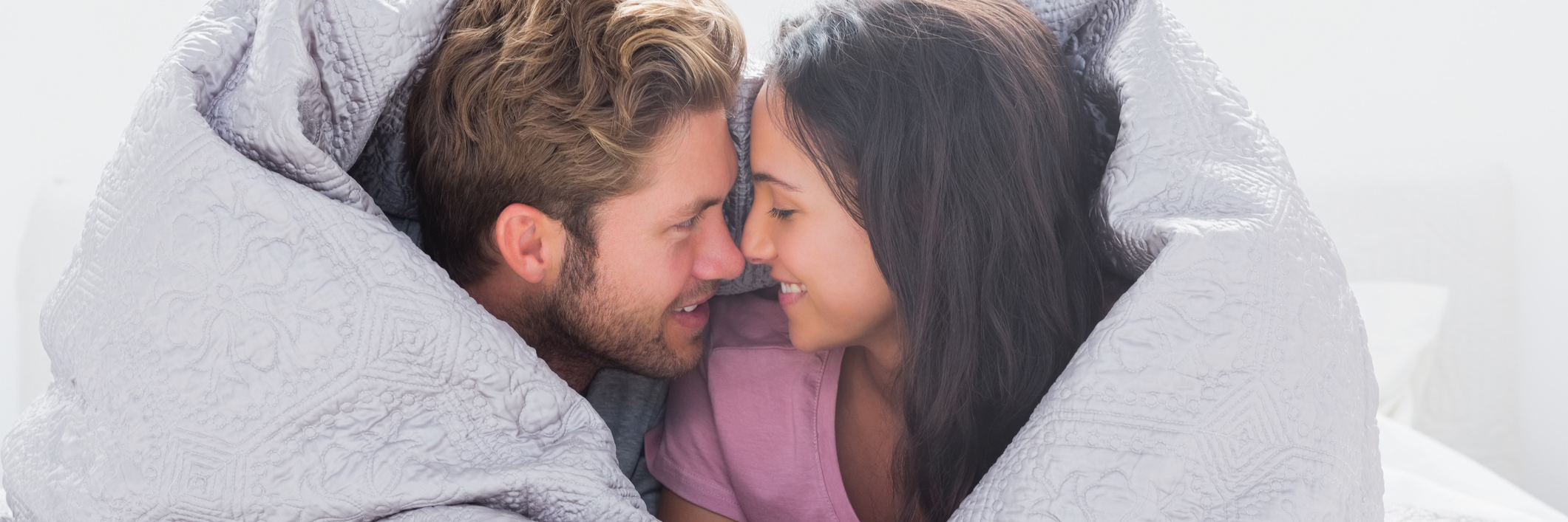 couple lying in bed wrapped in a duvet cover and smiling at each other