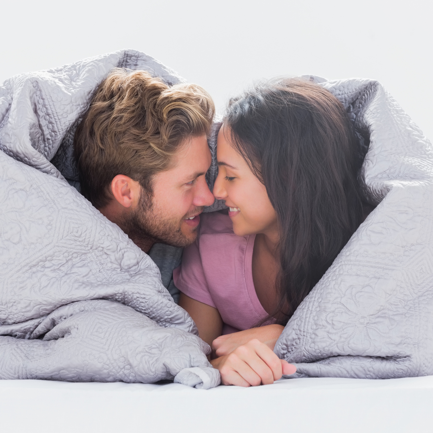 couple lying in bed wrapped in a duvet cover and smiling at each other