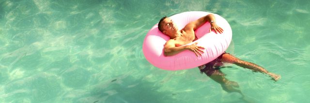 man lying in pink rubber ring in pool on summer day