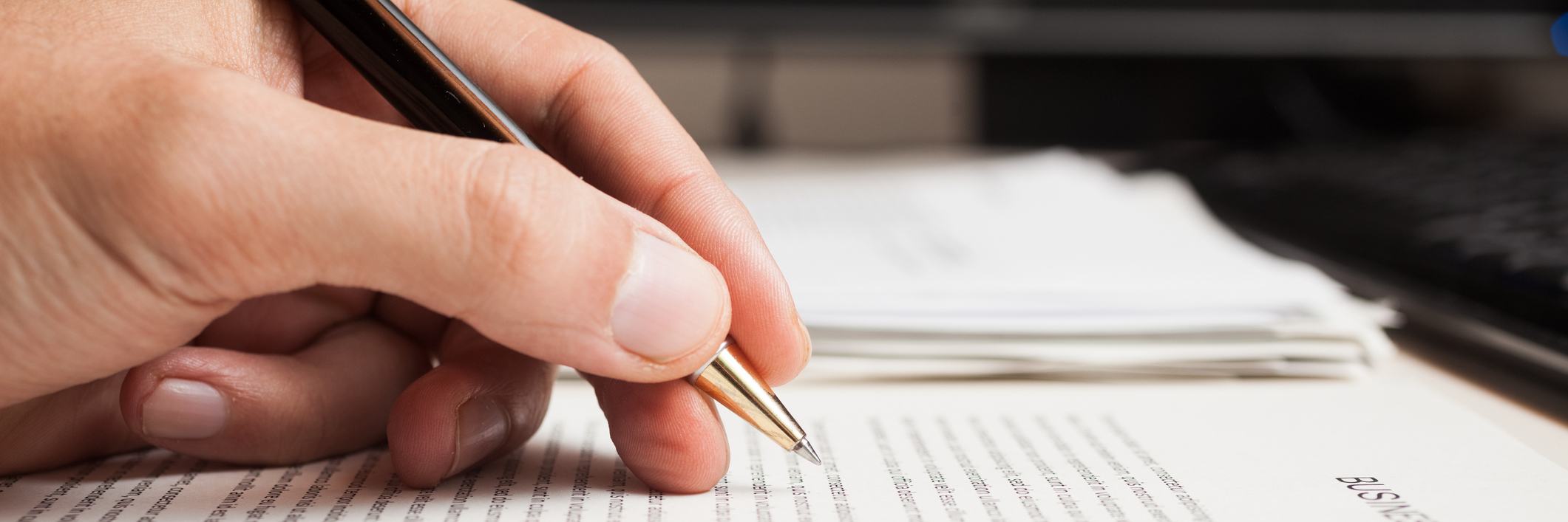 Improving Writing Skills With Dysgraphia Hand holding a pen on top of a pile of paperwork.