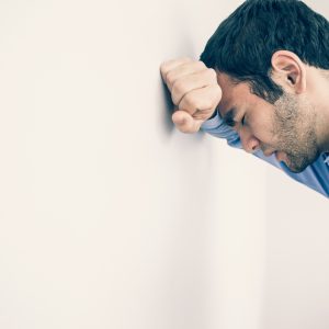 Man sad or depressed leaning against wall.