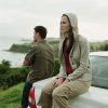 Young couple looking at coastline, woman sitting on back of car