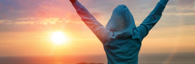 woman raising her arms in victory while looking at a sunset