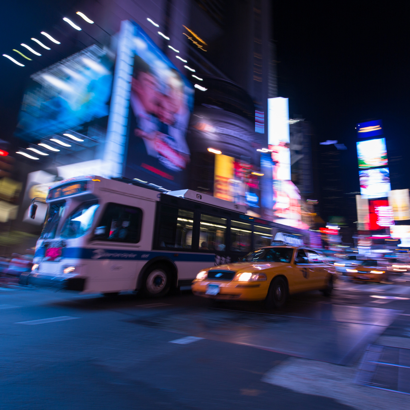 A long exposure night shot of a bus and a yellow cab driving through Times Square, NYC.