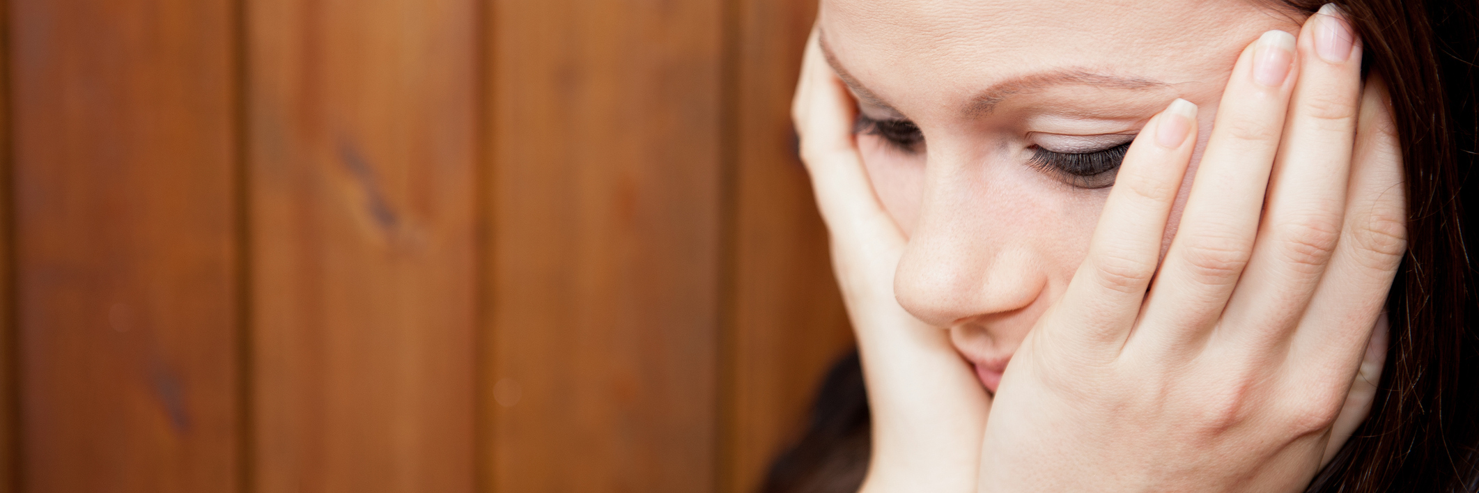 How Not to Deal With Anxiety Procrastination young woman head in hands looking worried against wooden wall backdrop