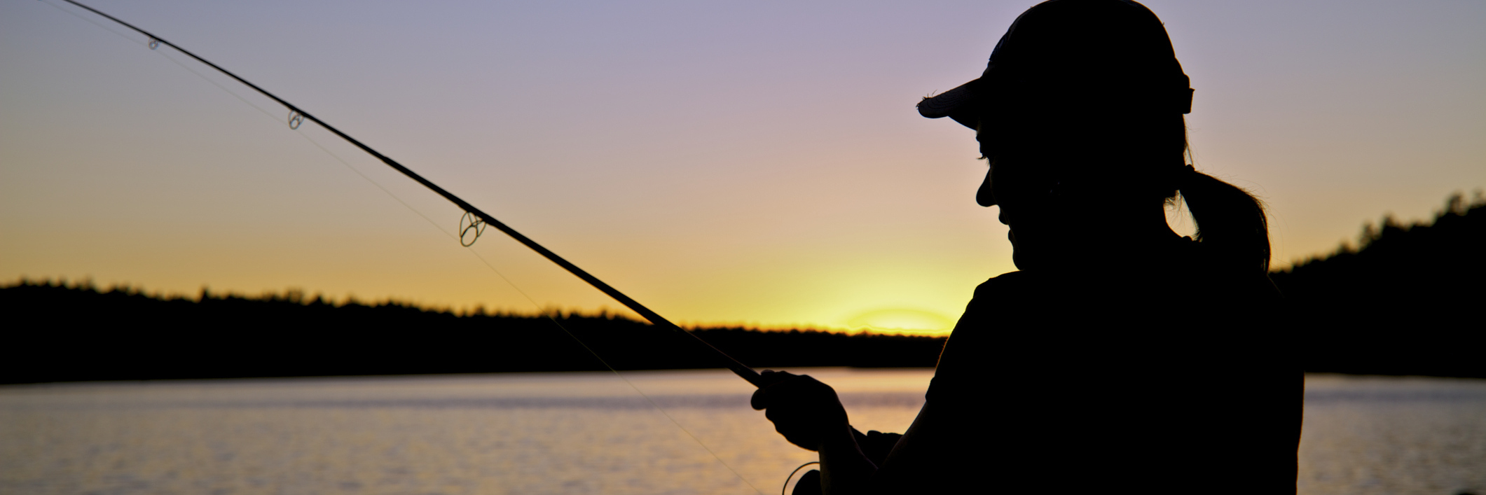 A woman fishing, silhouetted in the sunset.