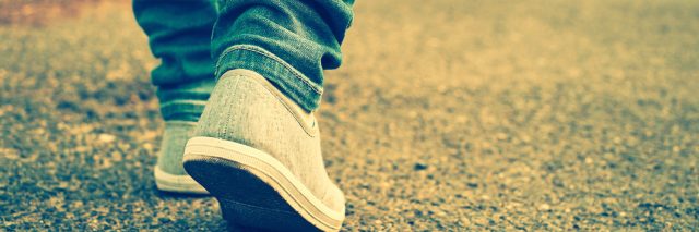 Close-up of person wearing jeans and shoes, walking on paved path