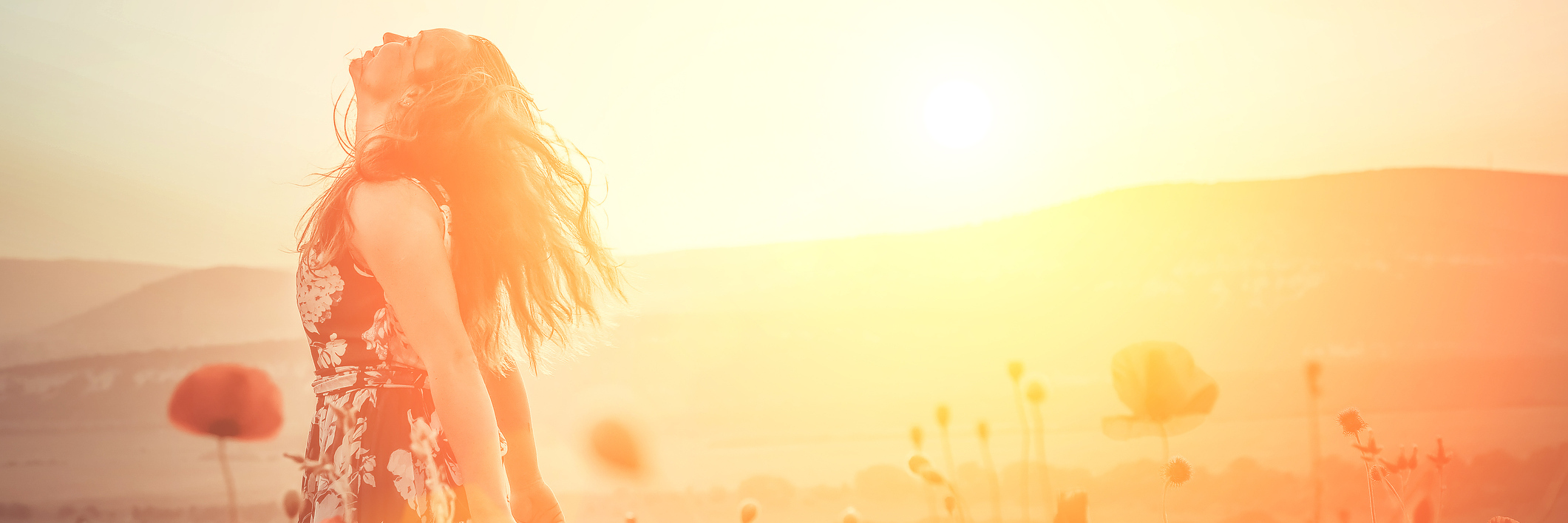 Why I Embrace My Strength That Was Created by Chronic Illness and Loss A woman in a field of flowers, the sun glowing from a distance.