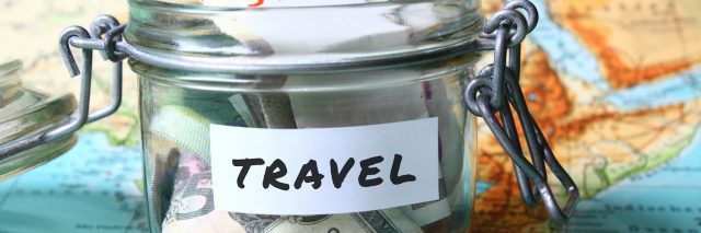 Glass jar with the word travel written on it and filled with money, on top of a world map