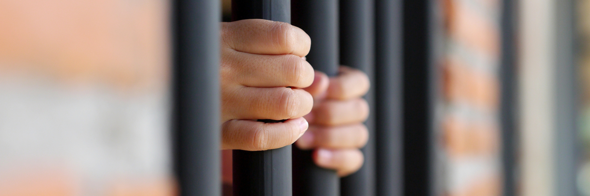 Female hands on jail bars, surrounded by a brick wall.