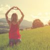 woman standing in field at sunset making heart shape with hands