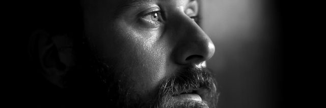 Close-up photo of a serious man with a beard in profile. Black and white image with shallow depth