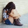 young sad girl sitting against a brick wall hugging her knees