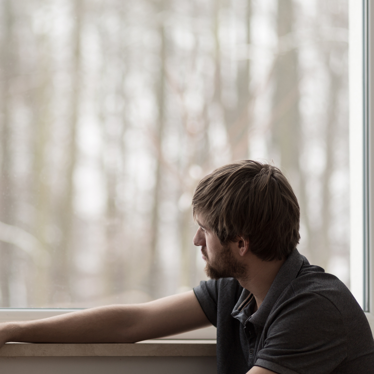 Young man who looks sad looking out the window at trees