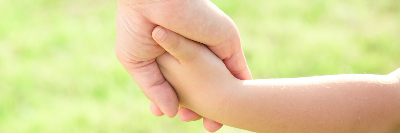 Close-up of mother and son holding hands on grass outdoors