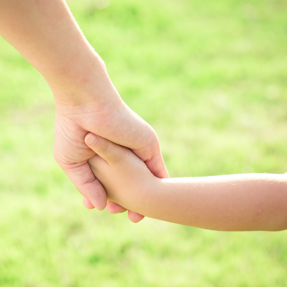 Close-up of mother and son holding hands on grass outdoors