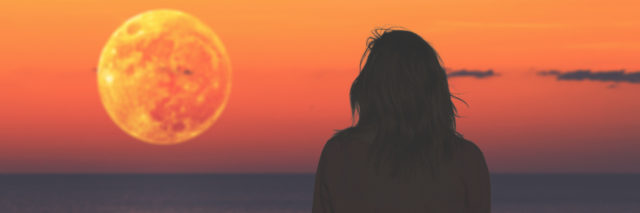 Woman watching the ocean as the moon rises.