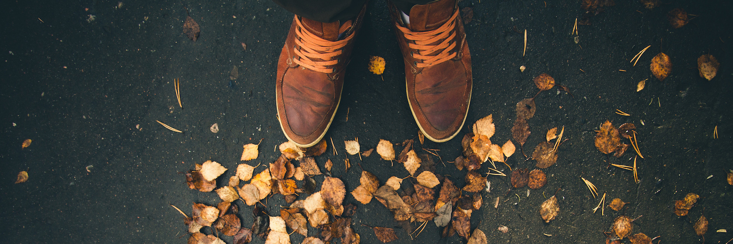 Close-up photo of two people's shoes facing each other with autumn leaves on the ground