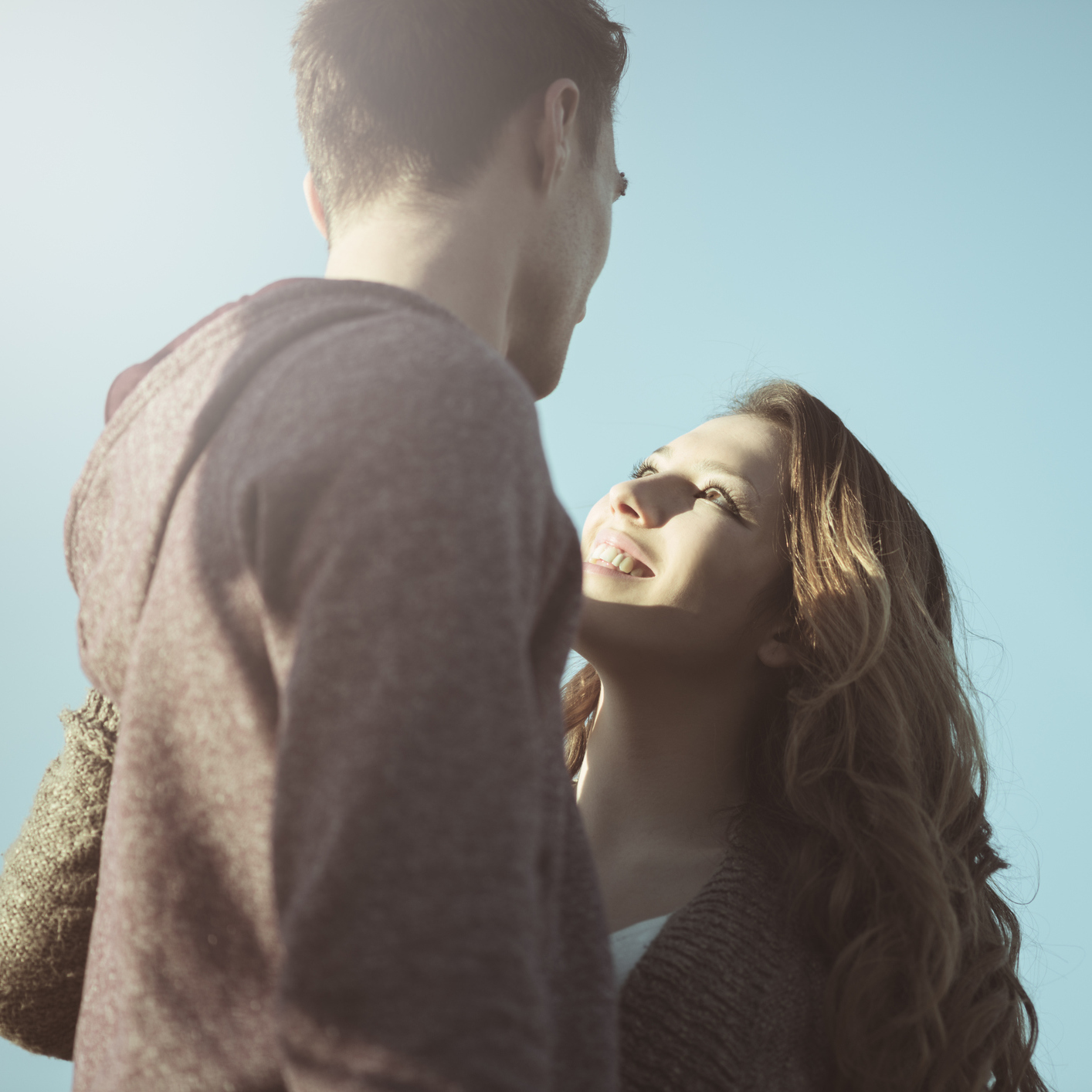 young couple outdoors against blue sky in sunlight looking at each other