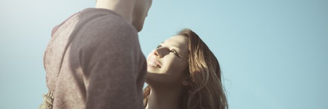 young couple outdoors against blue sky in sunlight looking at each other