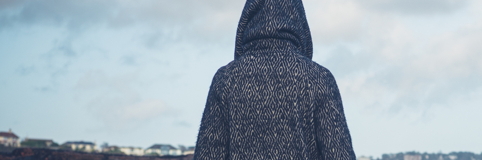 The Periods of Numbness That Come With My Grief Woman wearing hooded coat, walking on beach during gray, cloudy day