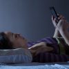 woman lying in bed at night checking her phone
