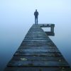 man standing alone on jetty over water on foggy day