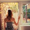 young woman standing at doorway of kitchen looking out at sunrise with arms and shoulders uncovered