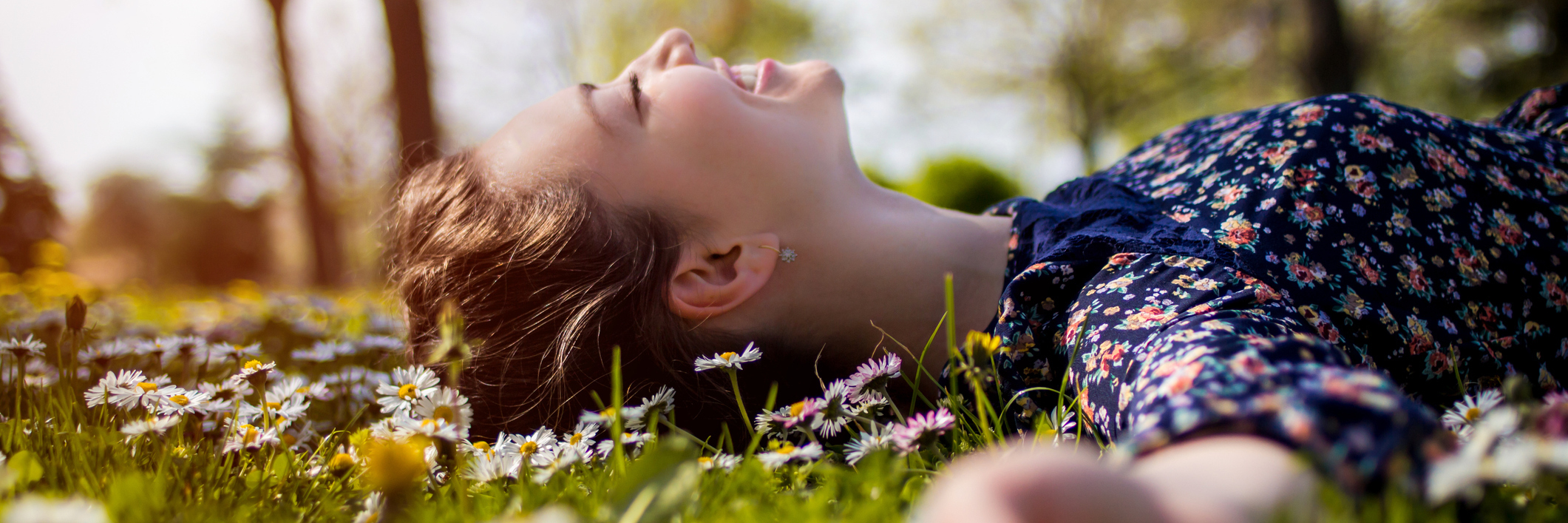 young girl lying on grass with daisies, smiling