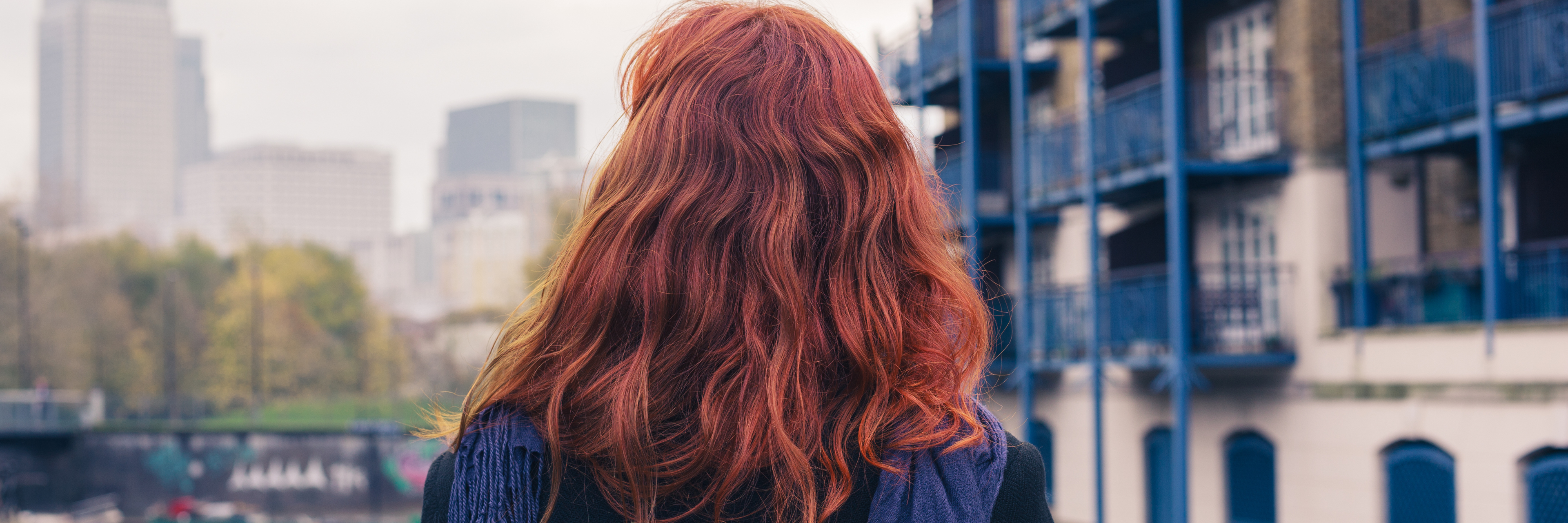 Letter to the Young Woman With Red Hair and Self-Harm Scars A young woman is walking outside and looking at buildings in the distance