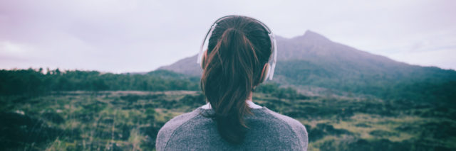 Woman in headphones listening to music while looking at a mountain.