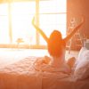 woman stretching in morning light while sitting up in bed