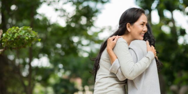 two asian women hugging in front of trees out of focus