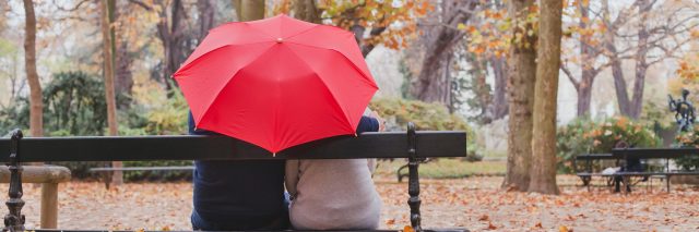 couple sitting on a park bench under a red umbrella